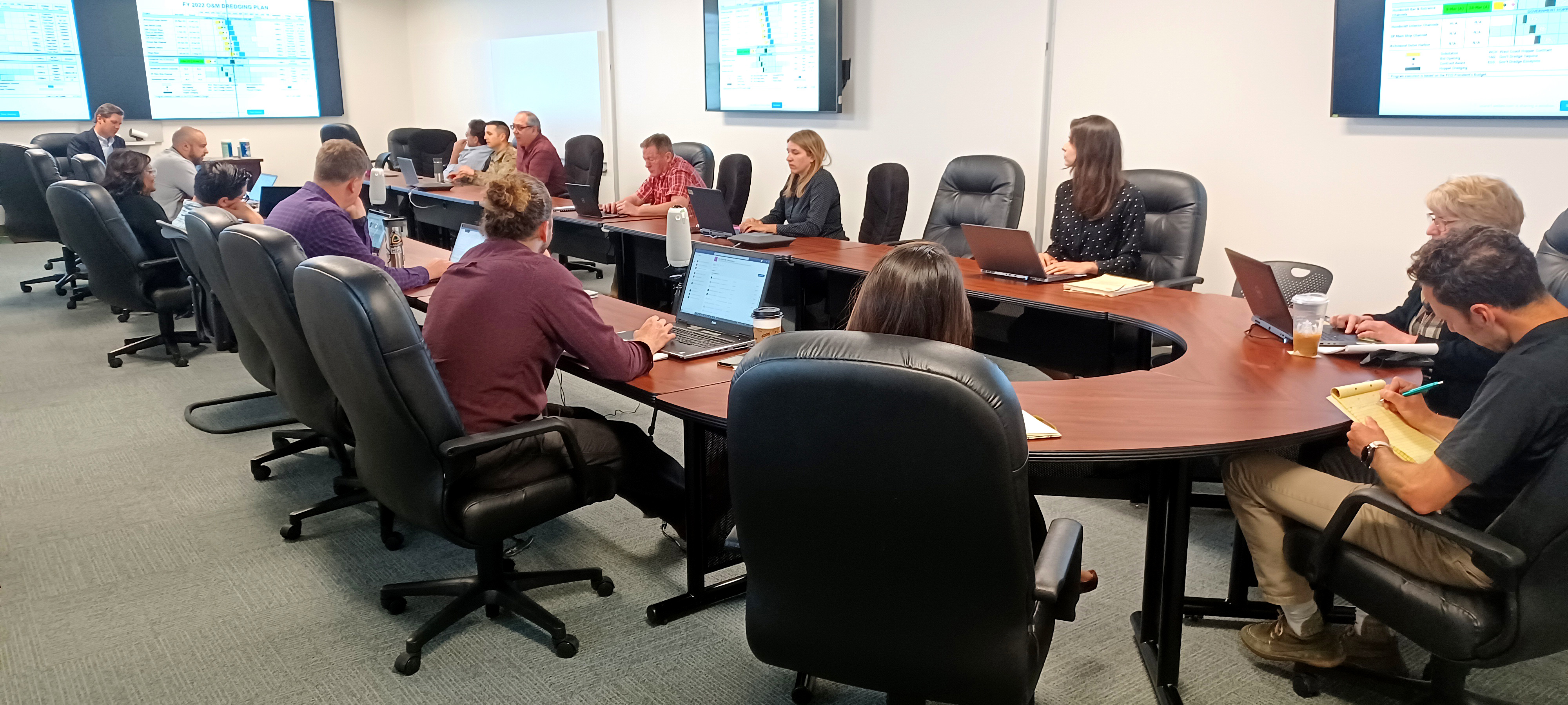 about 15 men and women sitting in a conference room around a u-shaped table. 